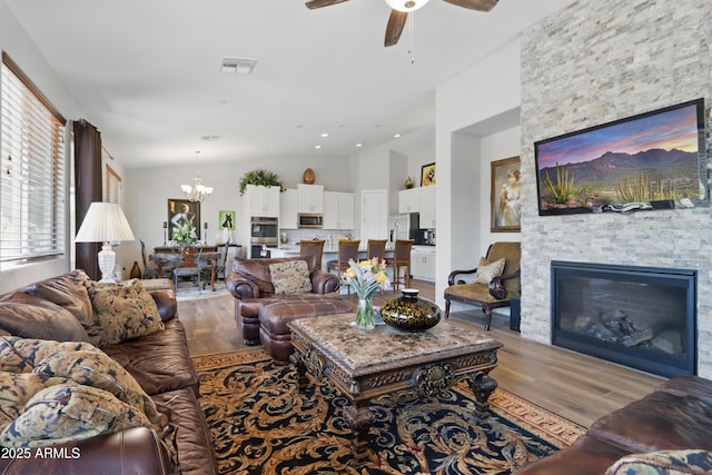19023 E Buckskin Ct, Rio Verde, AZ 85263 - living room with wood finished floors, a stone fireplace, lofted ceiling, ceiling fan with notable chandelier, and visible vents