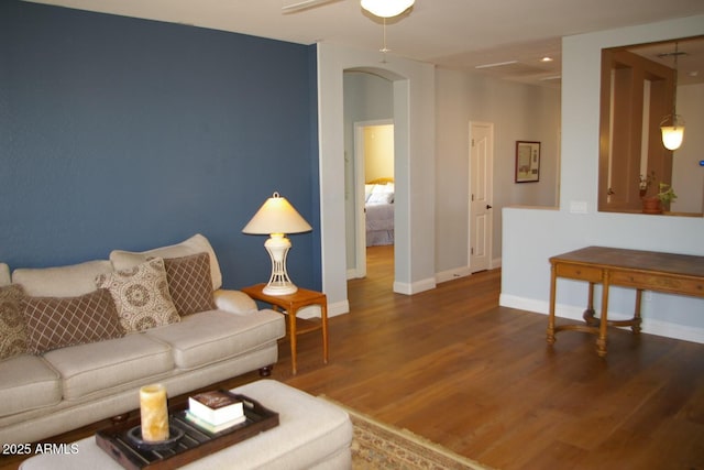 living room with baseboards, arched walkways, ceiling fan, and wood finished floors