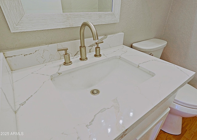 room details featuring toilet, a textured wall, wood finished floors, and vanity