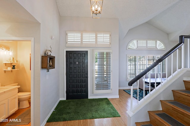 entrance foyer with light wood finished floors, baseboards, lofted ceiling, stairway, and a textured ceiling