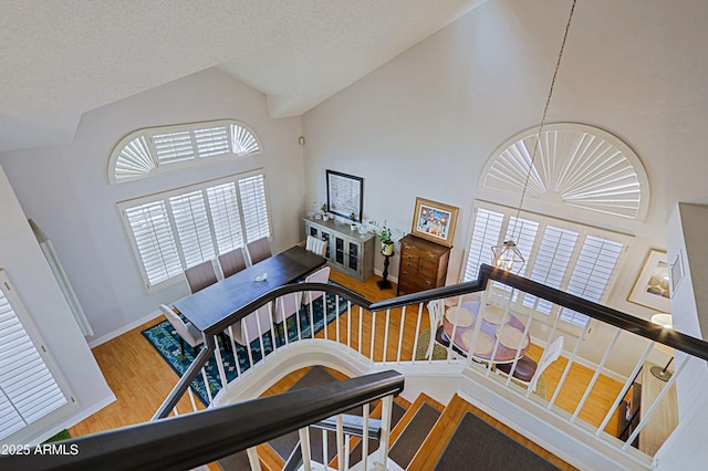 staircase with high vaulted ceiling, a textured ceiling, baseboards, and wood finished floors