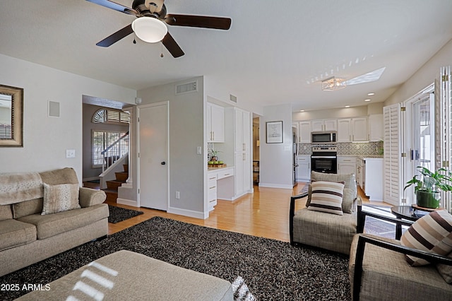 living area with stairs, baseboards, visible vents, and light wood-style floors