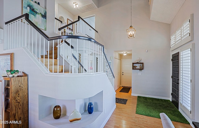 foyer featuring light wood-style flooring, a notable chandelier, a towering ceiling, baseboards, and stairs