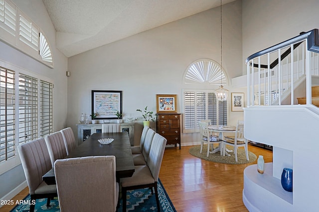 dining area with baseboards, high vaulted ceiling, wood finished floors, and an inviting chandelier