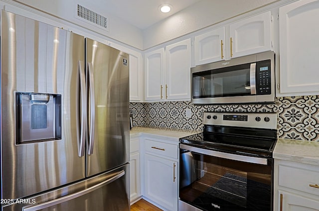 kitchen with appliances with stainless steel finishes, white cabinets, visible vents, and tasteful backsplash