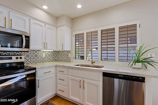 kitchen with appliances with stainless steel finishes, backsplash, a sink, and white cabinetry