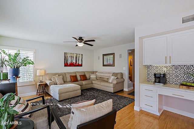 living area featuring ceiling fan, visible vents, baseboards, light wood-style floors, and built in desk