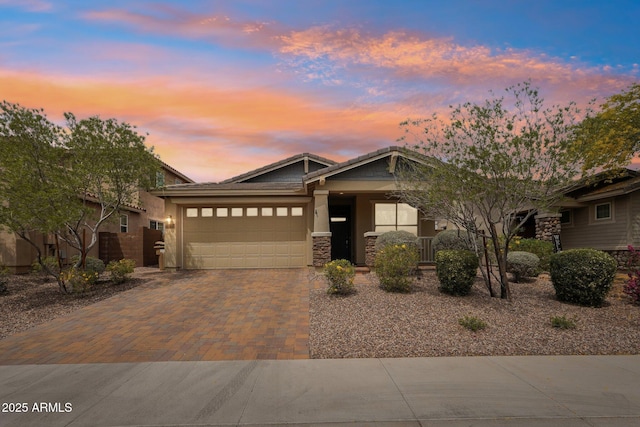 view of front of house featuring an attached garage, stone siding, a tile roof, stucco siding, and decorative driveway