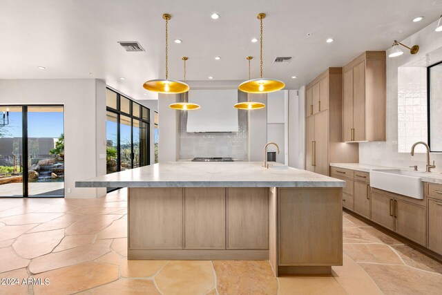 kitchen with backsplash, a center island with sink, decorative light fixtures, and sink