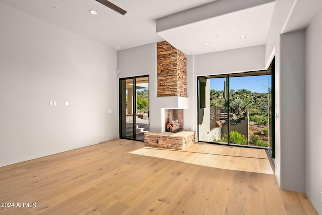 unfurnished living room featuring ceiling fan, a stone fireplace, and light hardwood / wood-style flooring