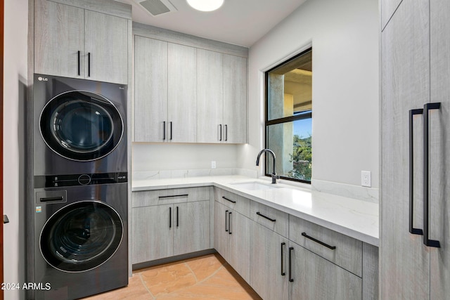 laundry room featuring light tile floors, cabinets, stacked washer and dryer, and sink