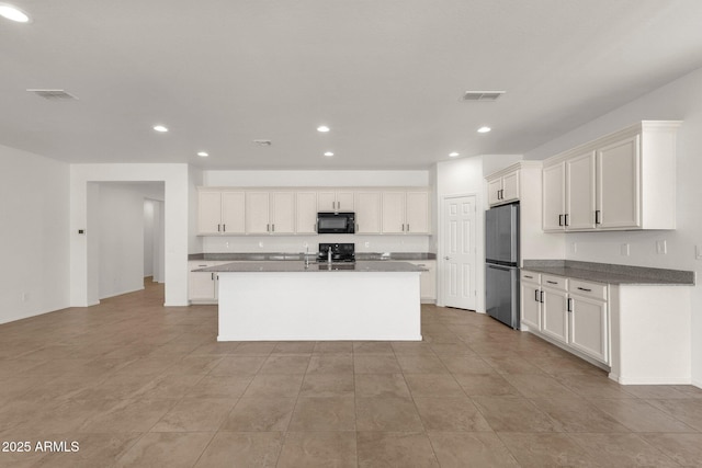 kitchen with visible vents, freestanding refrigerator, black microwave, white cabinetry, and recessed lighting