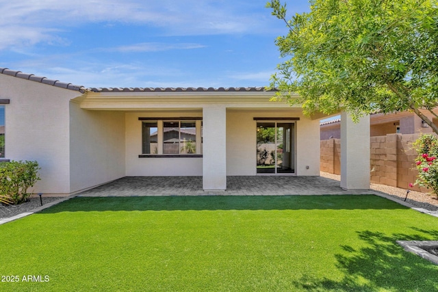 rear view of property featuring a yard, a tile roof, fence, and stucco siding