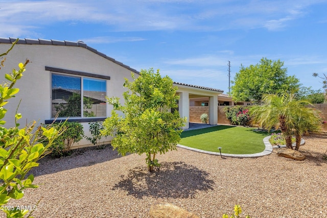 rear view of property featuring a tile roof, fence, a lawn, and stucco siding