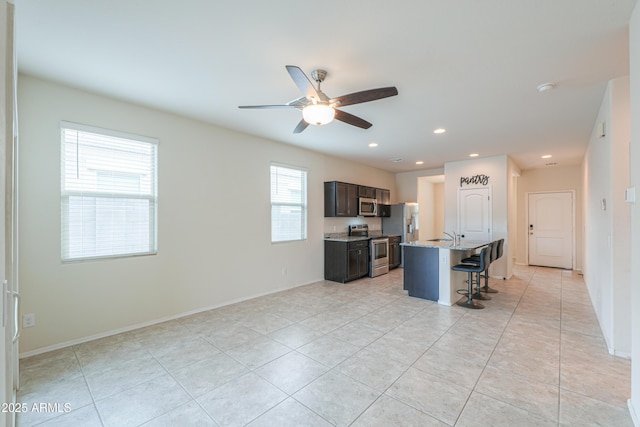 kitchen featuring a breakfast bar, ceiling fan, appliances with stainless steel finishes, a kitchen island with sink, and dark brown cabinetry