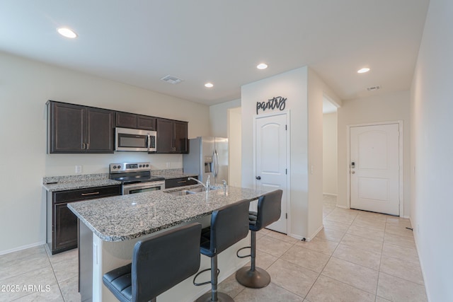 kitchen featuring a breakfast bar, sink, a kitchen island with sink, dark brown cabinetry, and stainless steel appliances