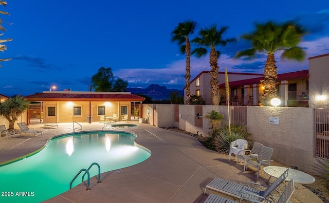 pool at dusk with a hot tub and a patio area