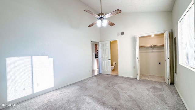 unfurnished bedroom featuring a spacious closet, high vaulted ceiling, a textured ceiling, a closet, and light colored carpet