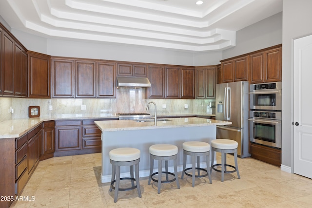 16246 E Gamble Ln, Scottsdale, AZ 85262 - kitchen featuring stainless steel appliances, a tray ceiling, under cabinet range hood, a breakfast bar, and backsplash