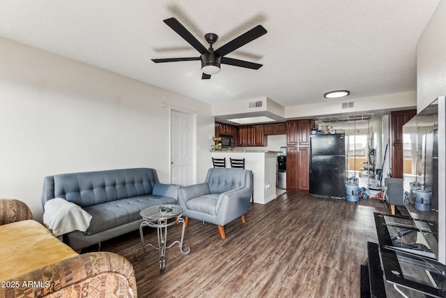 living area with dark wood-style flooring, visible vents, ceiling fan, and a textured ceiling