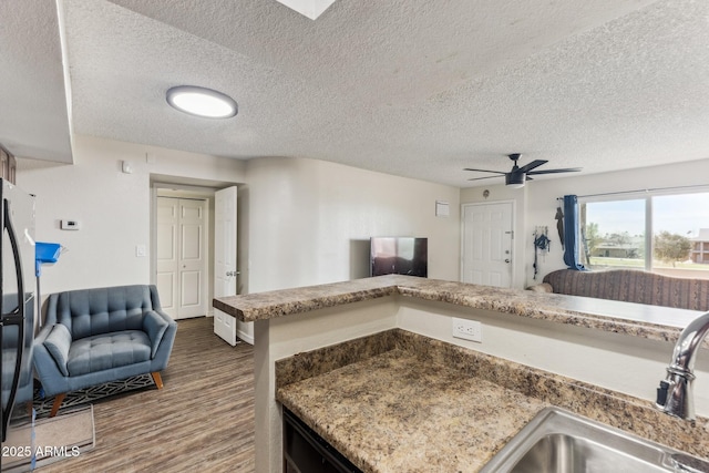 kitchen with dark wood-style flooring, freestanding refrigerator, open floor plan, a sink, and a textured ceiling