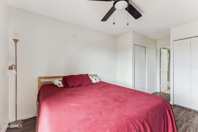 bedroom with dark wood-style floors, ceiling fan, and two closets