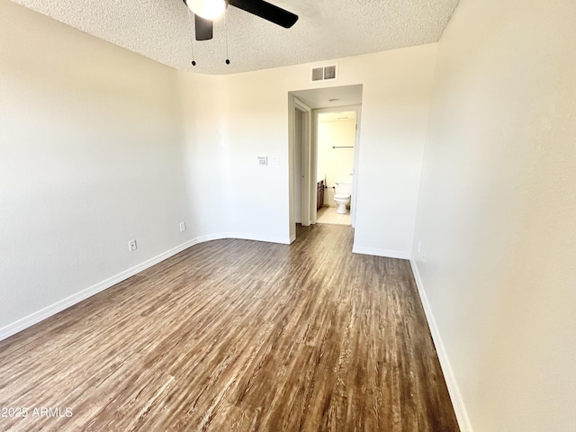 empty room featuring dark wood-style floors, visible vents, baseboards, a textured ceiling, and ceiling fan