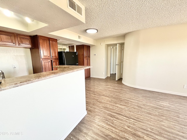 kitchen with light countertops, wood finished floors, visible vents, freestanding refrigerator, and baseboards