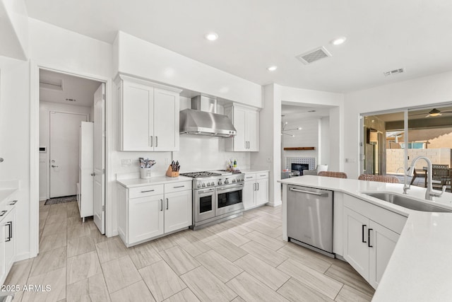 kitchen with light countertops, stainless steel appliances, wall chimney exhaust hood, a ceiling fan, and a sink