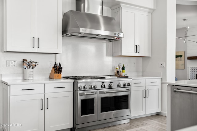 kitchen featuring light wood finished floors, wall chimney range hood, light countertops, appliances with stainless steel finishes, and white cabinets