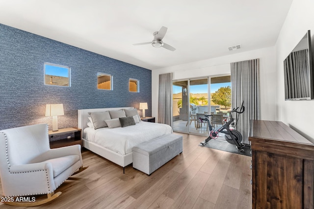 bedroom featuring wood finished floors, visible vents, wallpapered walls, an accent wall, and access to outside