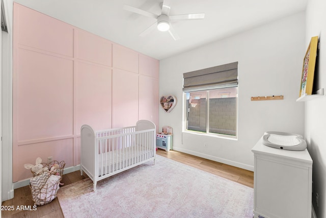 bedroom with a nursery area, baseboards, light wood-style floors, and ceiling fan