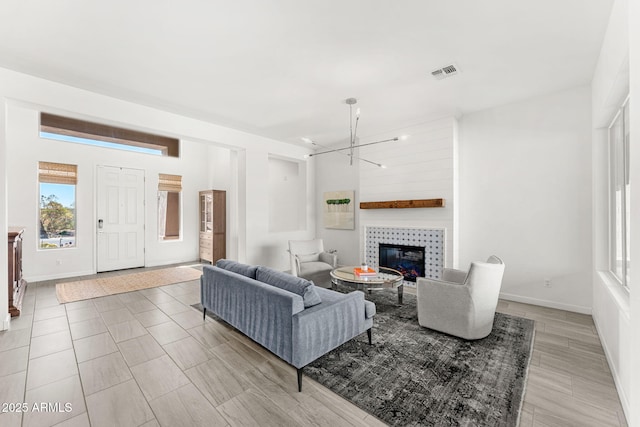 living area with an inviting chandelier, a fireplace, visible vents, and baseboards