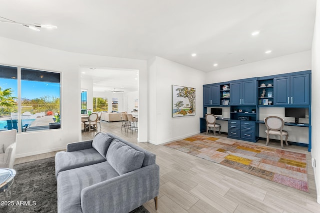 living area featuring a ceiling fan, baseboards, light wood-style flooring, recessed lighting, and built in desk