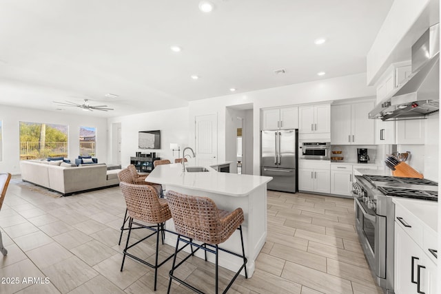 kitchen featuring a breakfast bar area, high end appliances, a sink, light countertops, and wall chimney range hood