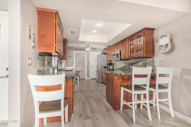 kitchen with kitchen peninsula, decorative backsplash, a tray ceiling, light wood-type flooring, and stainless steel appliances