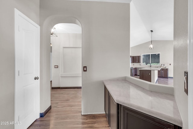 interior space featuring arched walkways, lofted ceiling, light countertops, light wood finished floors, and pendant lighting