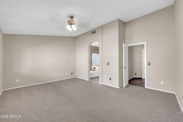 unfurnished bedroom featuring arched walkways, carpet floors, visible vents, and baseboards