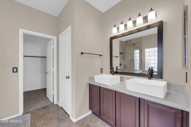 full bath featuring a tile shower, double vanity, a sink, and baseboards