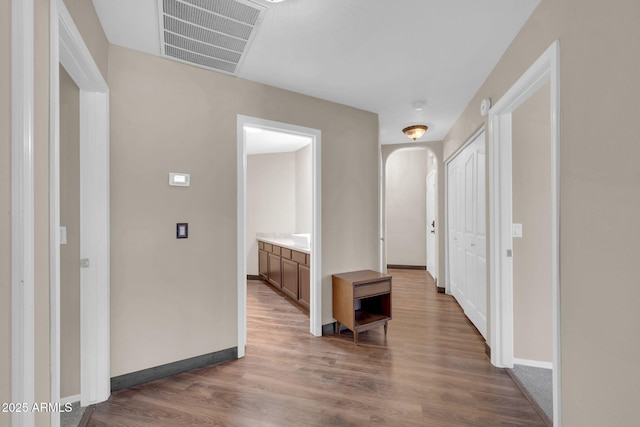 hall with arched walkways, wood finished floors, visible vents, and baseboards