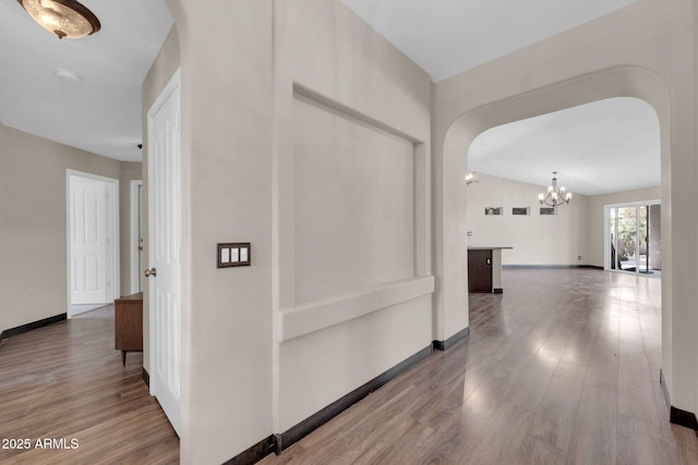 hall featuring arched walkways, an inviting chandelier, baseboards, and wood finished floors