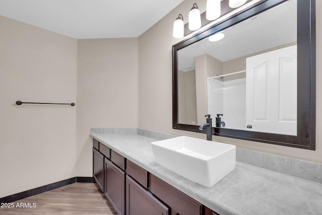 bathroom with a shower, vanity, baseboards, and wood finished floors