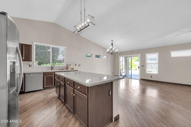 kitchen featuring light wood-style flooring, vaulted ceiling, light countertops, appliances with stainless steel finishes, and a center island