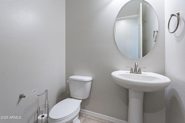 half bath featuring toilet, a textured wall, tile patterned flooring, and baseboards