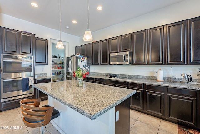 kitchen with appliances with stainless steel finishes, decorative light fixtures, light stone counters, a kitchen breakfast bar, and light tile patterned floors