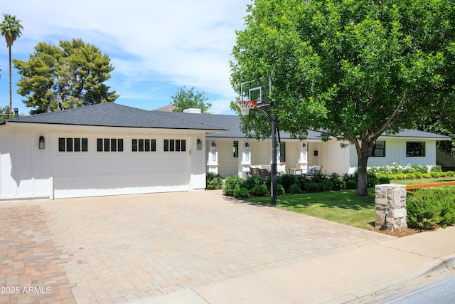 view of front of house with decorative driveway, a front lawn, board and batten siding, a garage, and roof with shingles