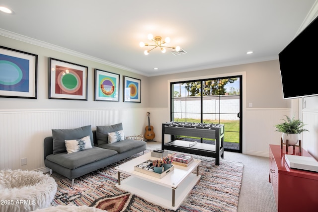 living area featuring a wainscoted wall, visible vents, a chandelier, and ornamental molding