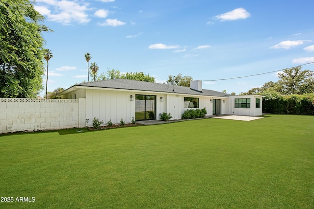 back of house with fence, a shingled roof, board and batten siding, a patio, and a lawn