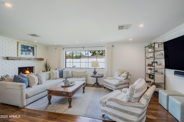 living area featuring a brick fireplace, wood finished floors, visible vents, and crown molding