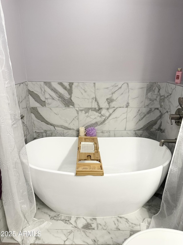 bathroom with marble finish floor and a soaking tub